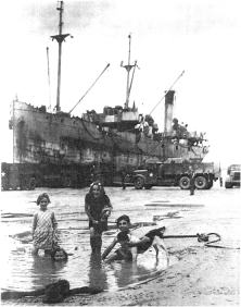 (détails) Un caboteur décharge directement dans l'avant-port marée basse, pendant que des enfants jouent. Cela s'est passé à l'époque où le port d'OImaha Beach était hors